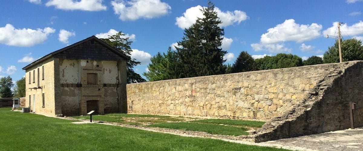 A historic stone wall and a weathered building with a grassy field in front.