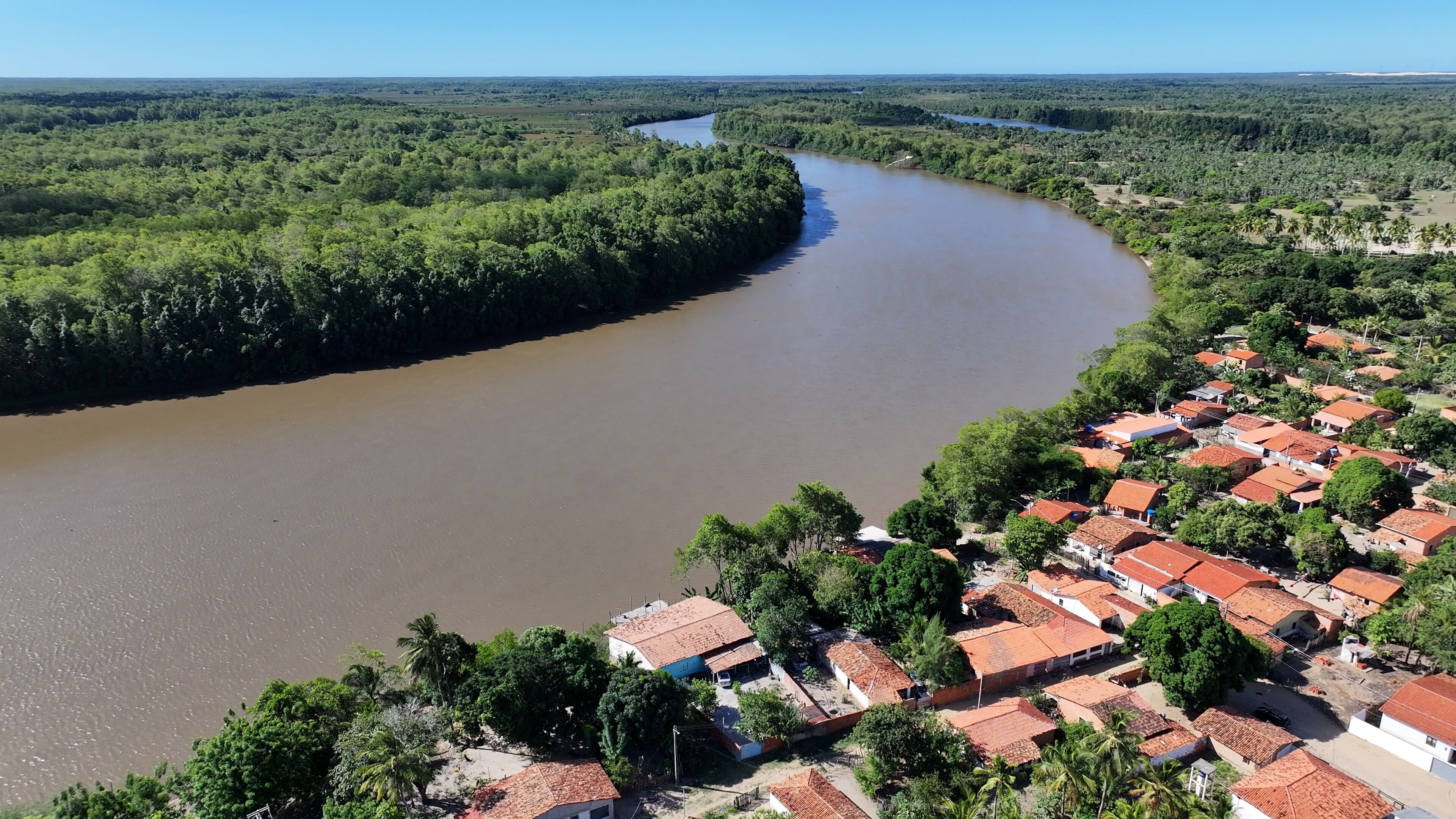 A river curving through a densely forested area with a small settlement of red-roofed houses.