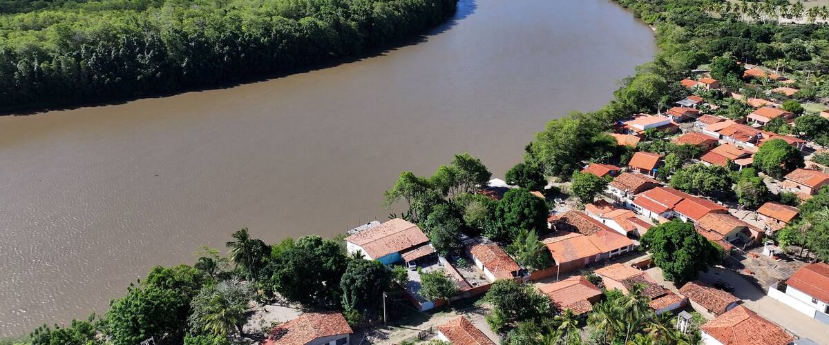 A river curving through a densely forested area with a small settlement of red-roofed houses.
