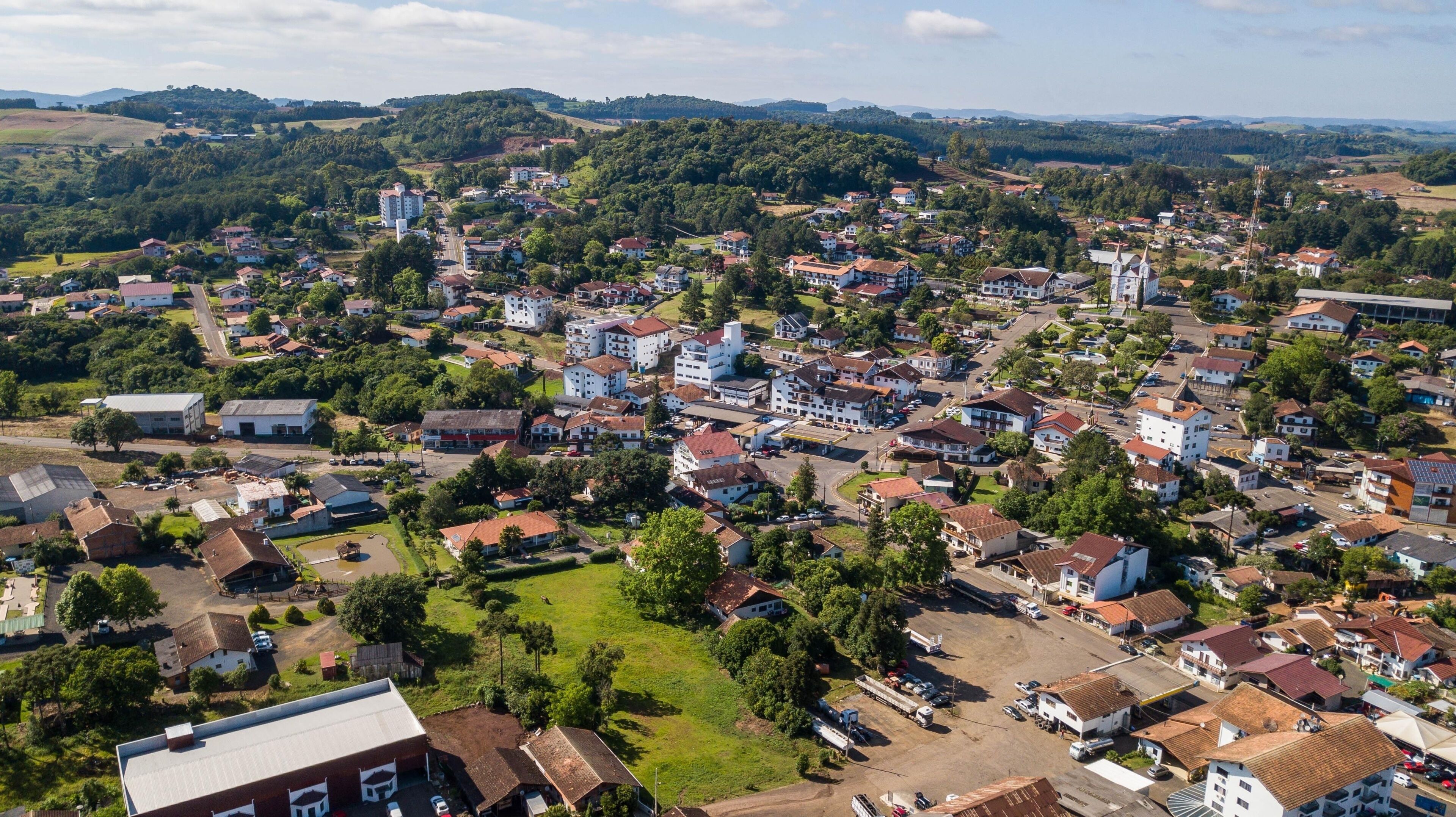 A town with a mix of residential and commercial buildings, surrounded by green hills and a clear sky.