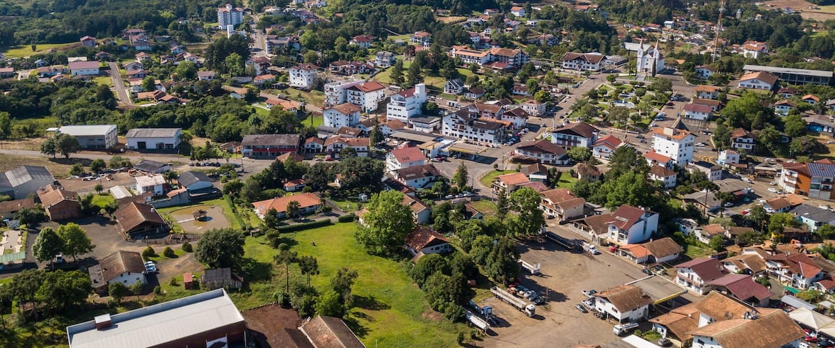 A town with a mix of residential and commercial buildings, surrounded by green hills and a clear sky.