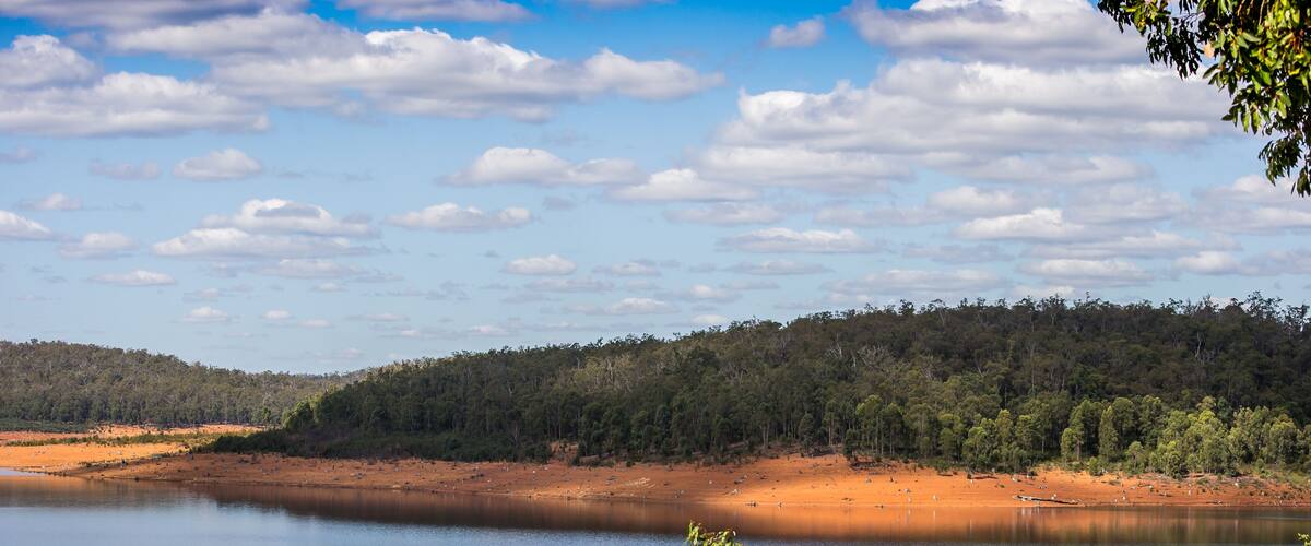 A lake with a rocky shoreline and a forested hill in the background.