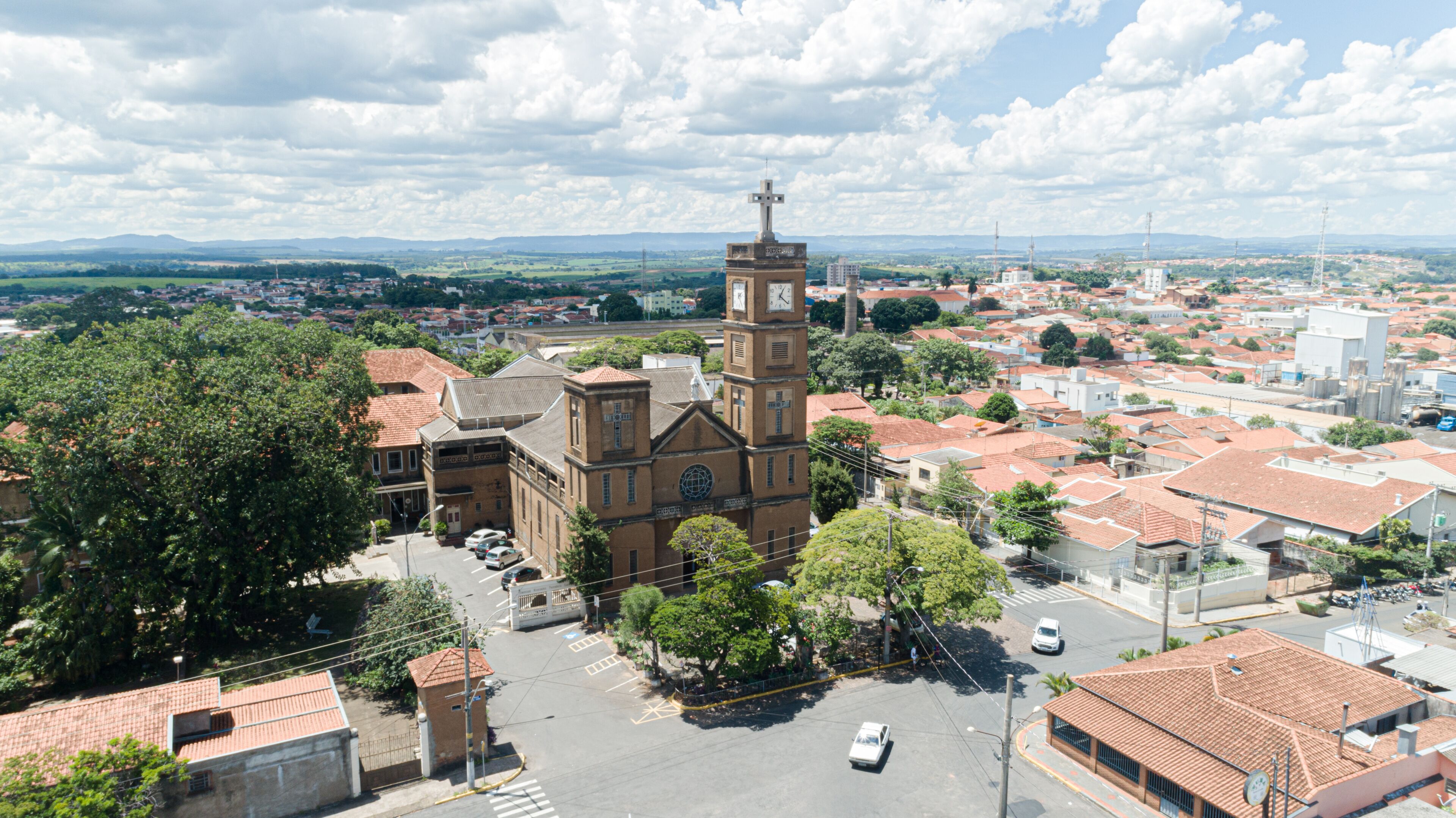 A church with a clock tower, surrounded by a town with red-roofed buildings and green trees.
