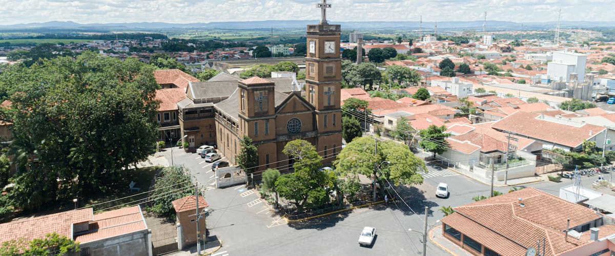 A church with a clock tower, surrounded by a town with red-roofed buildings and green trees.
