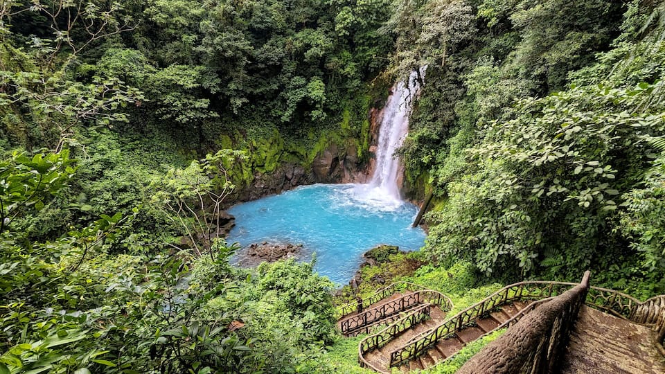 A waterfall in a lush green forest with a clear blue pool at its base.