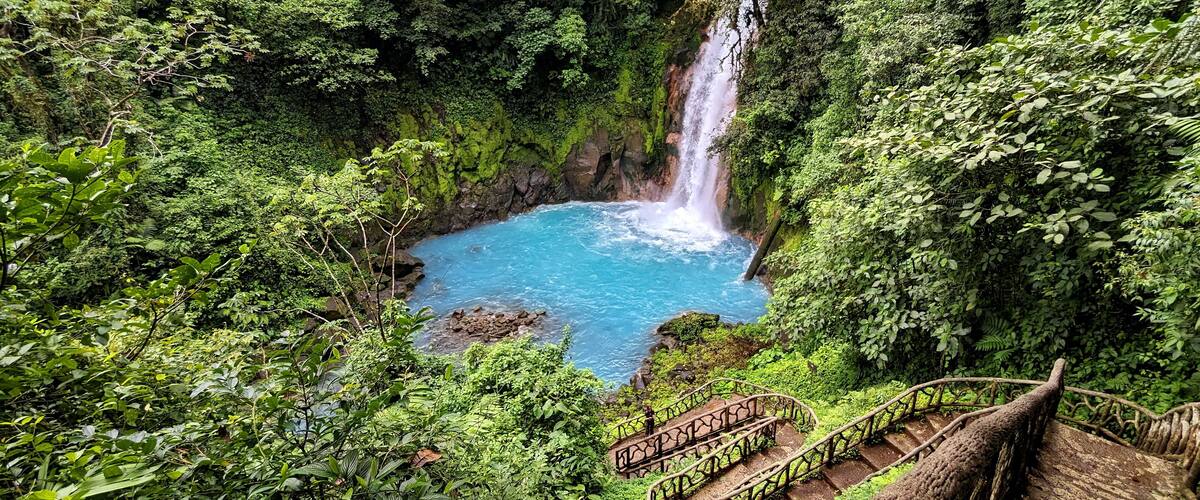 A waterfall in a lush green forest with a clear blue pool at its base.