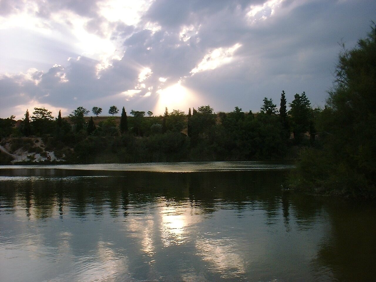 A calm lake with trees reflecting the sunlight.