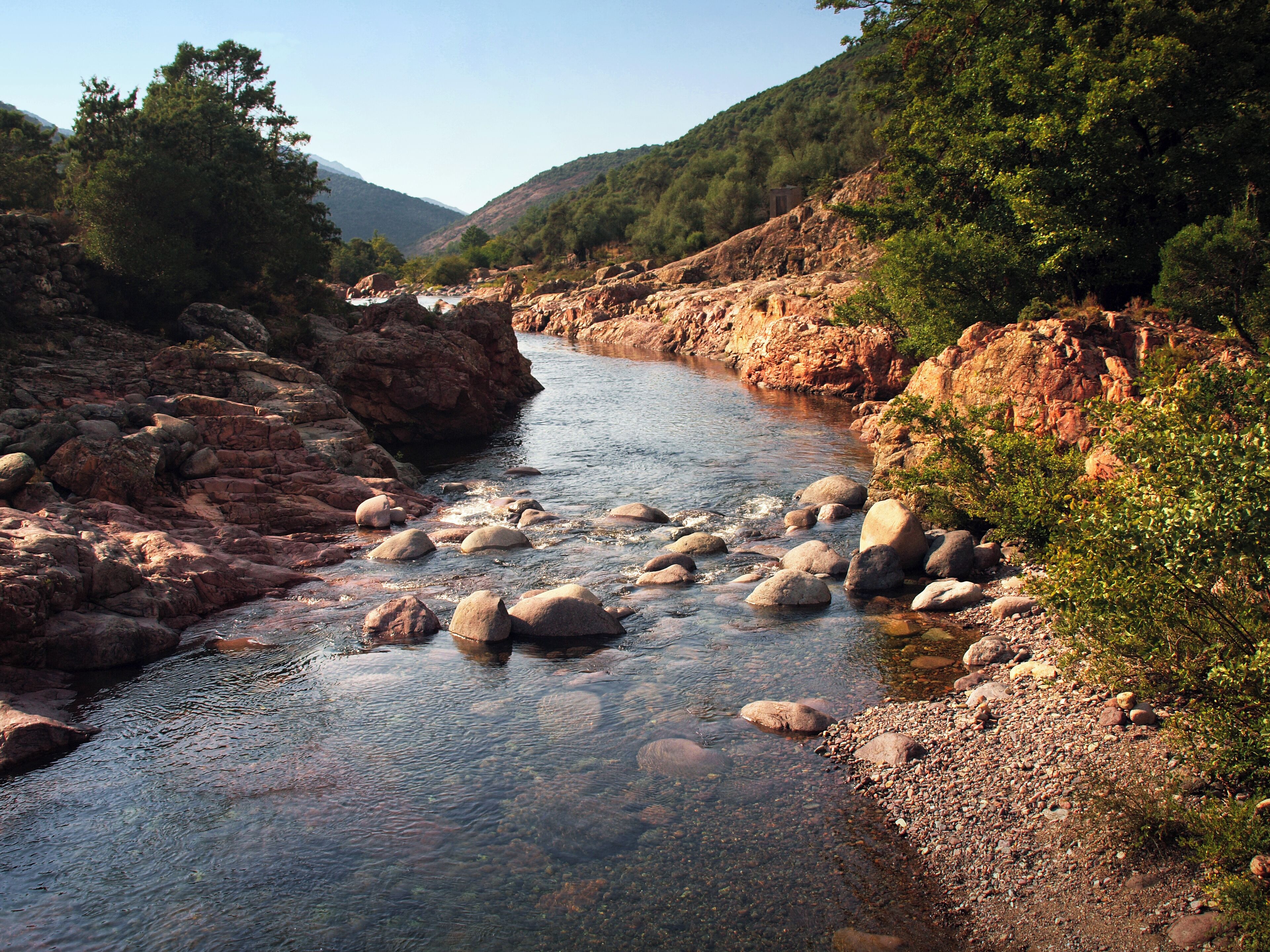 A river with clear water, surrounded by rocky terrain and greenery.