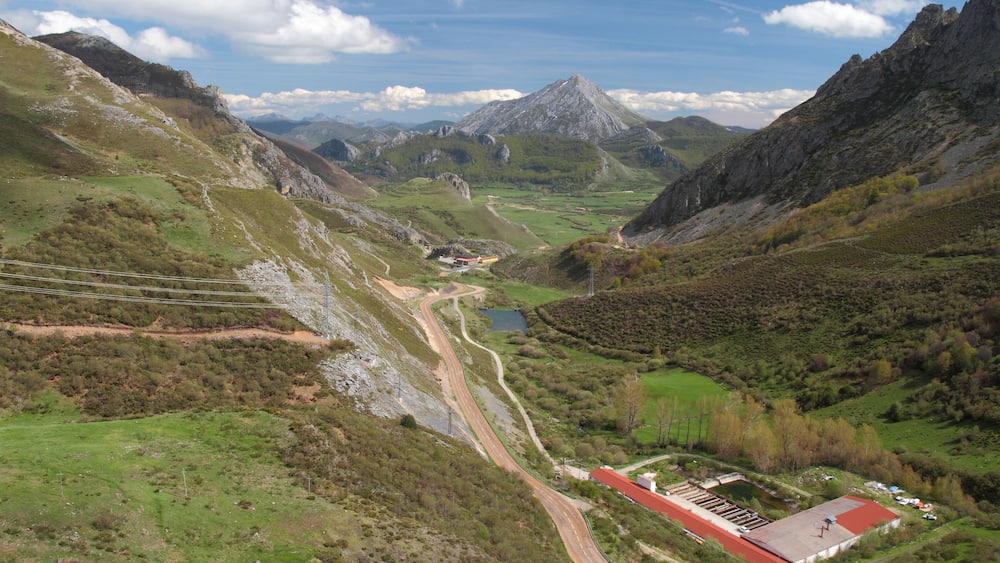 A mountainous landscape with a winding road, a small building with a red roof, and a lake in the valley.