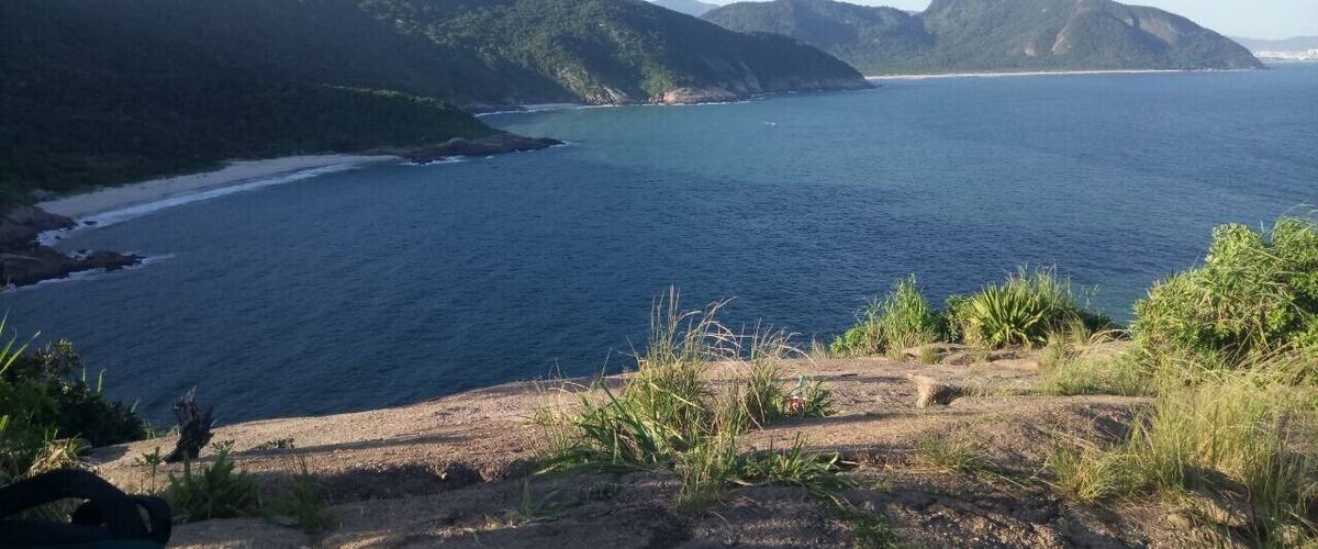 A coastal landscape with a beach, clear blue sea, and green hills.