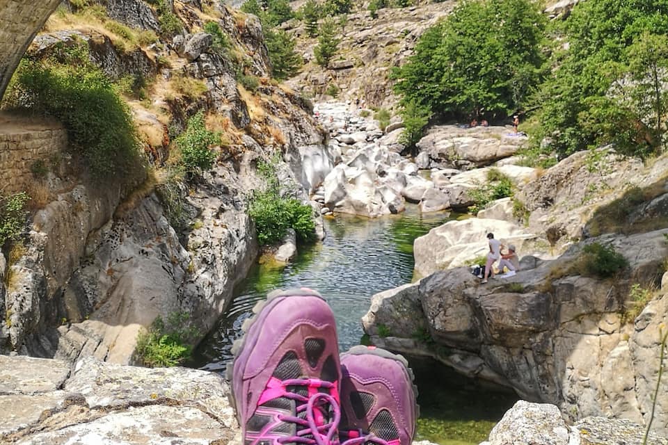 Un puente de piedra en arco que cruza un río, con montañas al fondo.