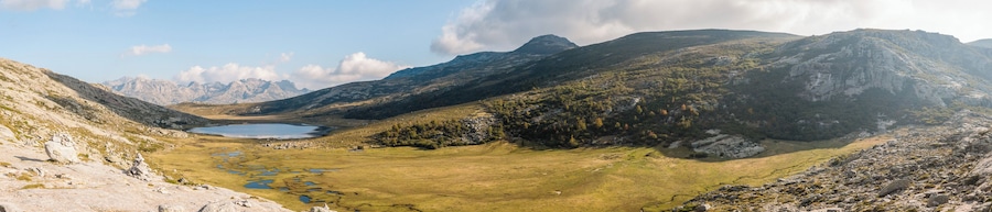 A mountainous landscape with a lake, rocky terrain, and sparse vegetation.