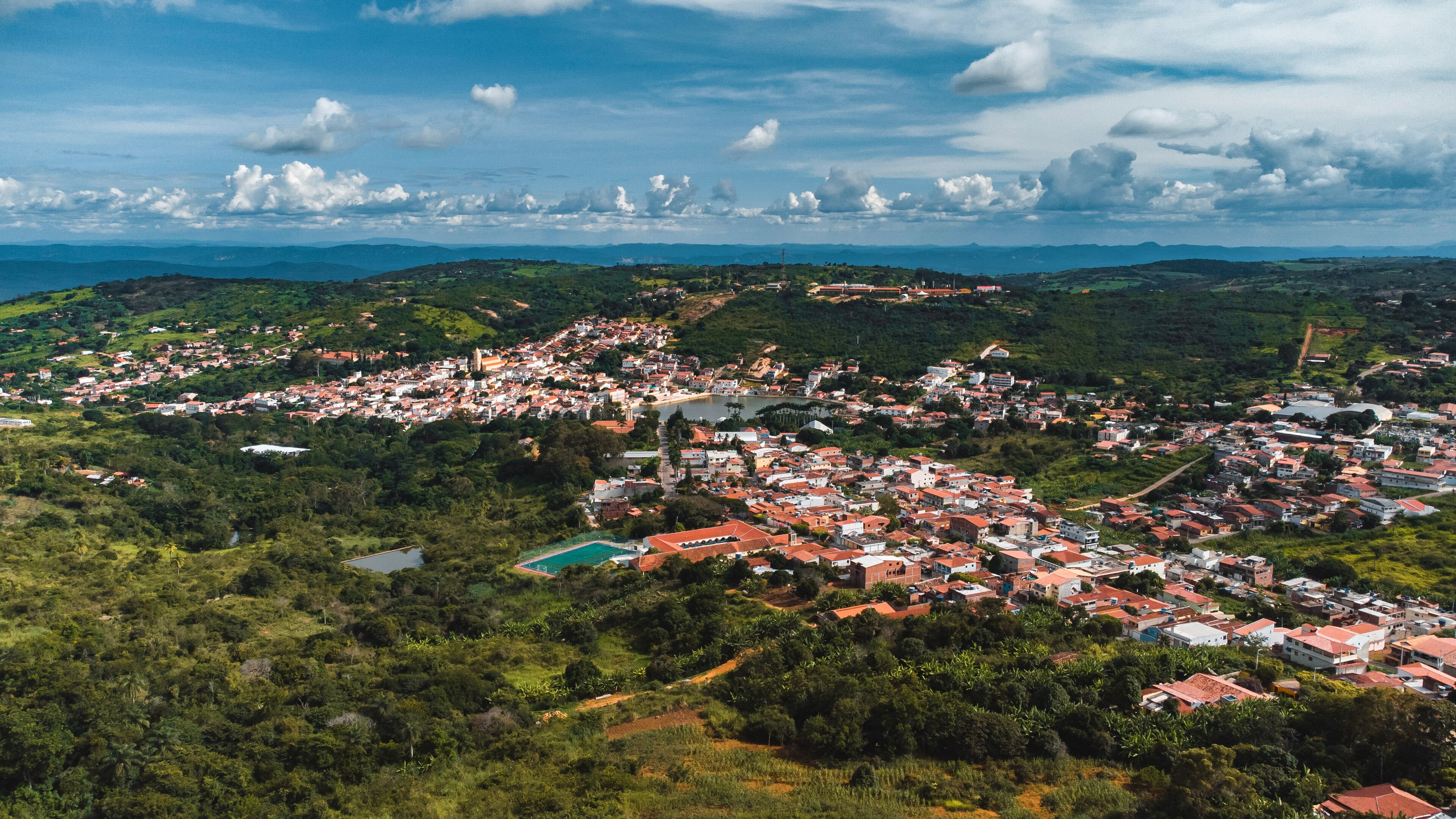 A coastal town with red-roofed buildings, a beach, and surrounding hills.