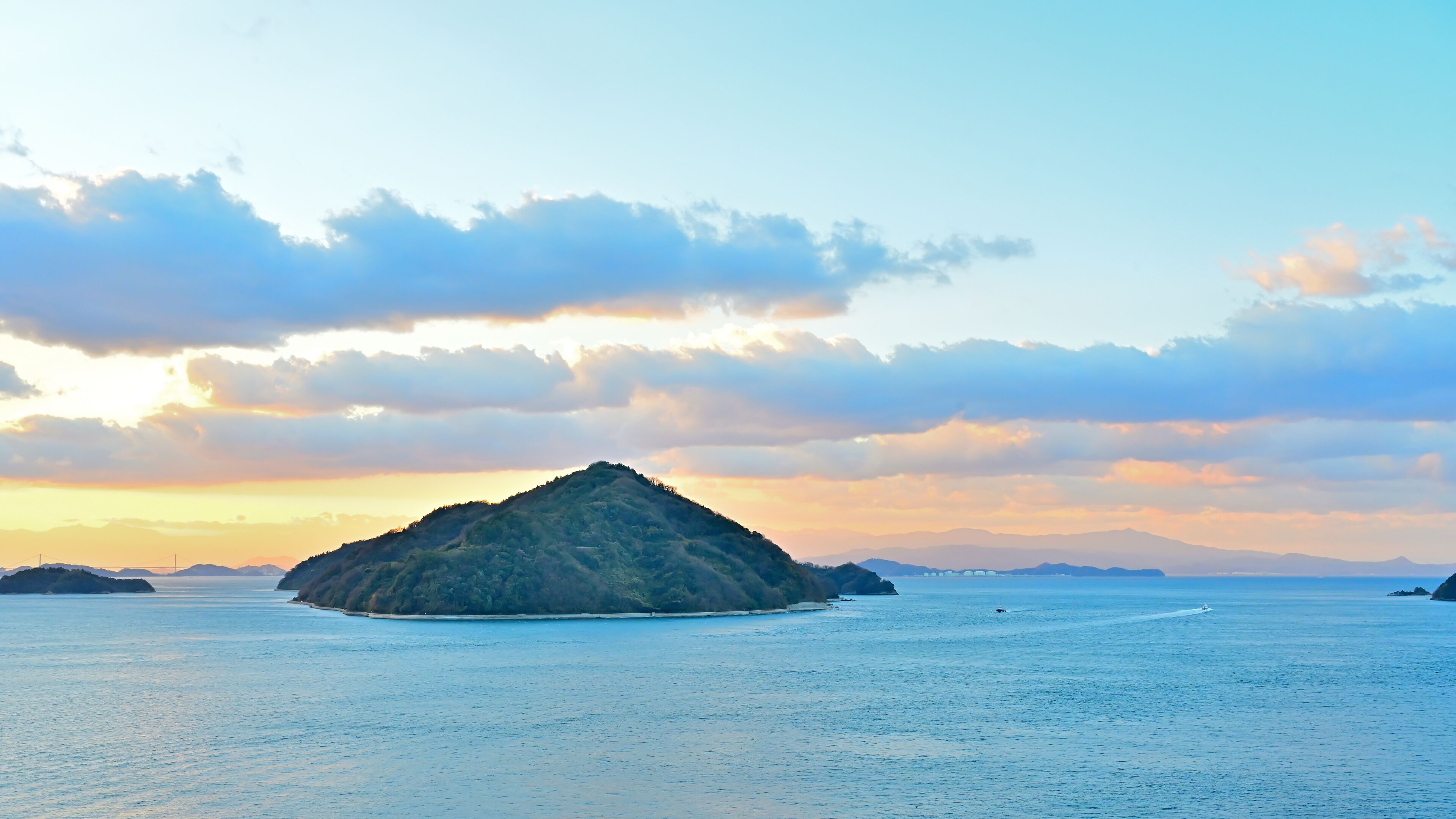 A small island surrounded by calm waters with a clear sky and distant mountains.