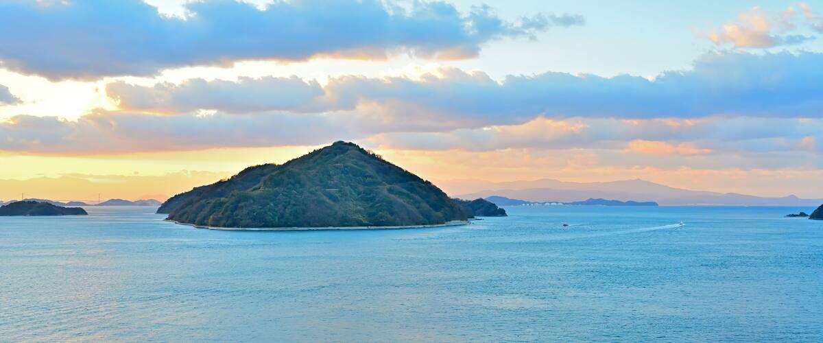 A small island surrounded by calm waters with a clear sky and distant mountains.