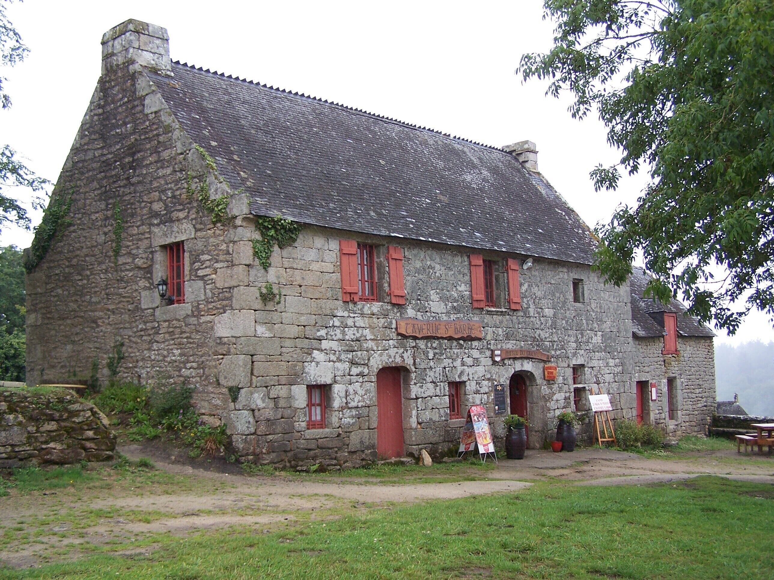 A stone building with red shutters and a sign reading "Caverne St Barbe".
