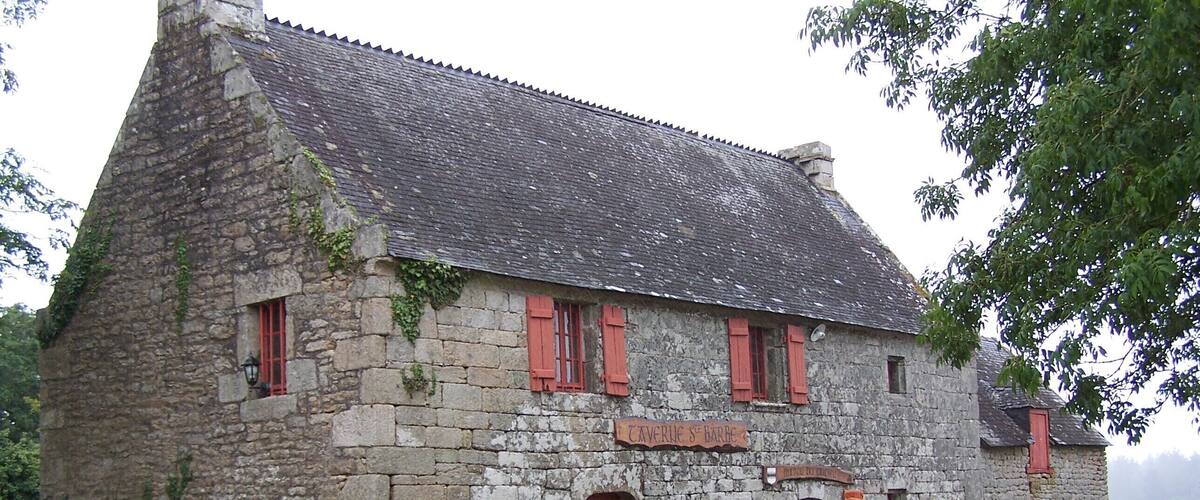 A stone building with red shutters and a sign reading "Caverne St Barbe".