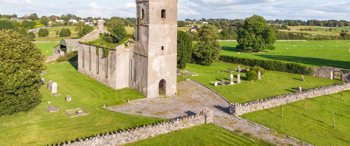 A historic stone tower with a battlement, surrounded by a well-maintained cemetery and lush green fields.