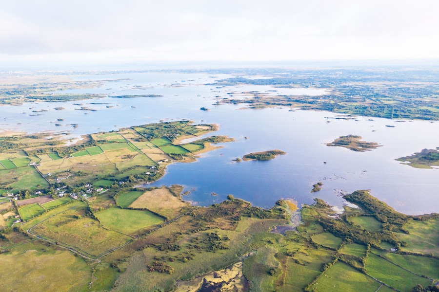 An aerial view of a coastal landscape with fields, small islands, and a large body of water.