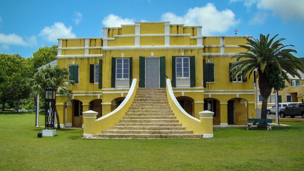 A yellow building with a central staircase and green shutters.