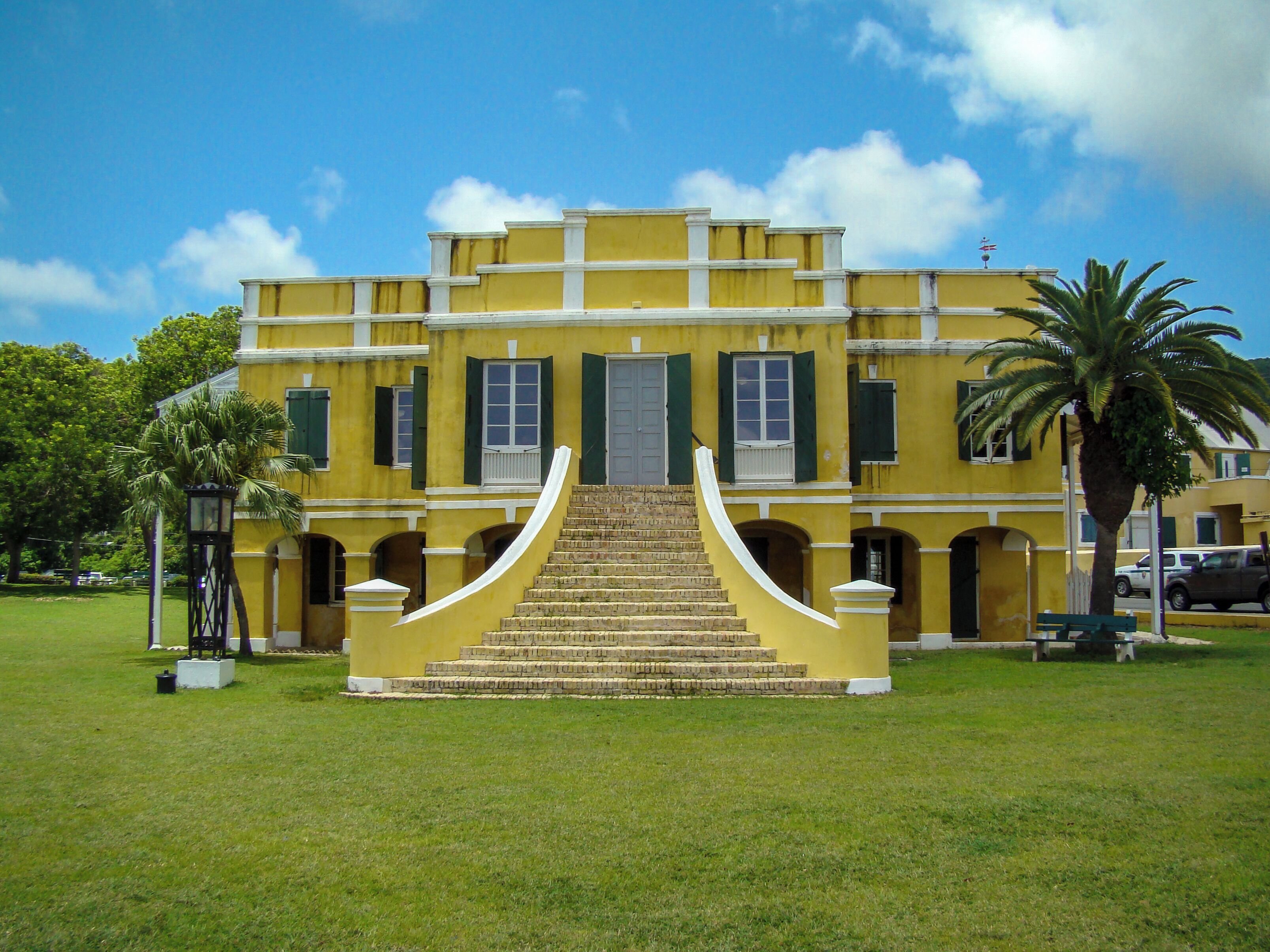 A yellow building with a central staircase and green shutters.