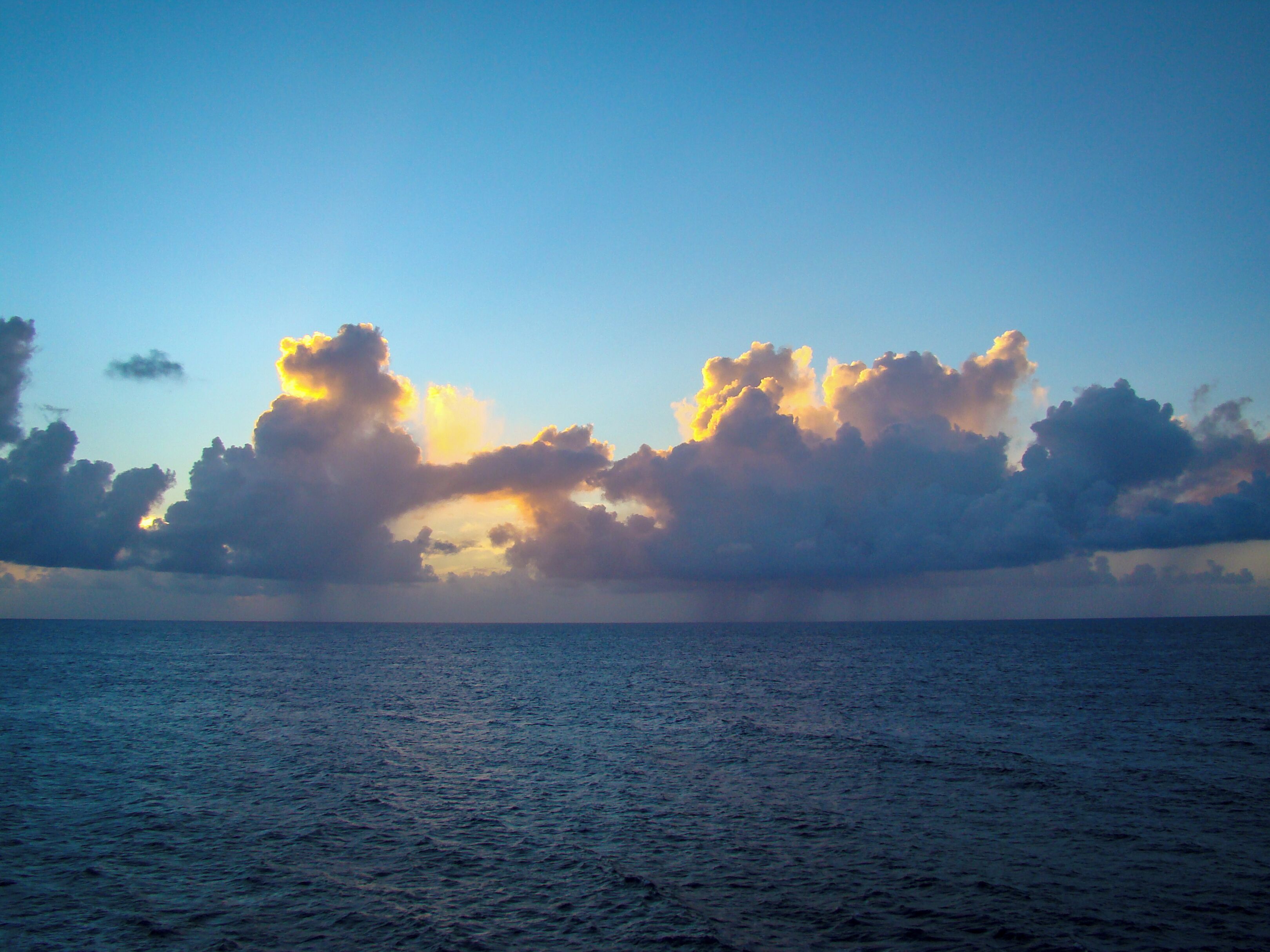 A calm sea with a clear sky and scattered clouds.