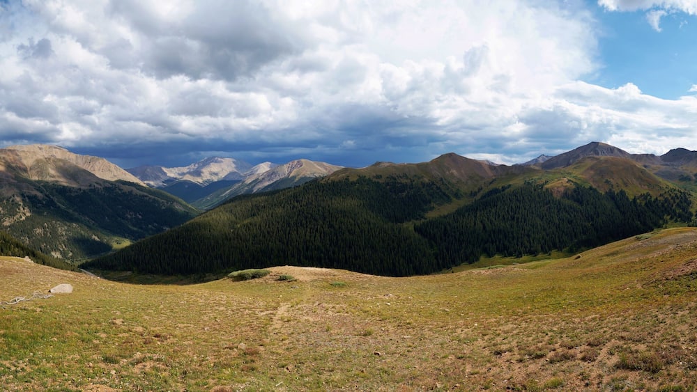 A mountainous landscape with a valley, forested slopes, and a clear sky.