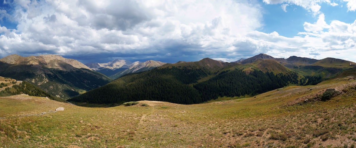 A mountainous landscape with a valley, forested slopes, and a clear sky.
