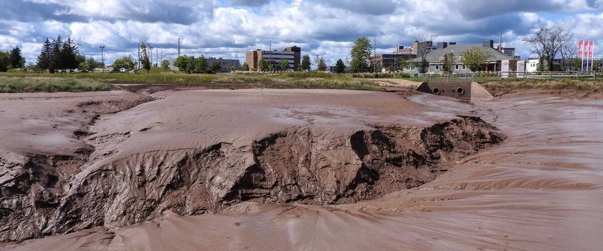 A flooded area with muddy terrain and buildings in the background.