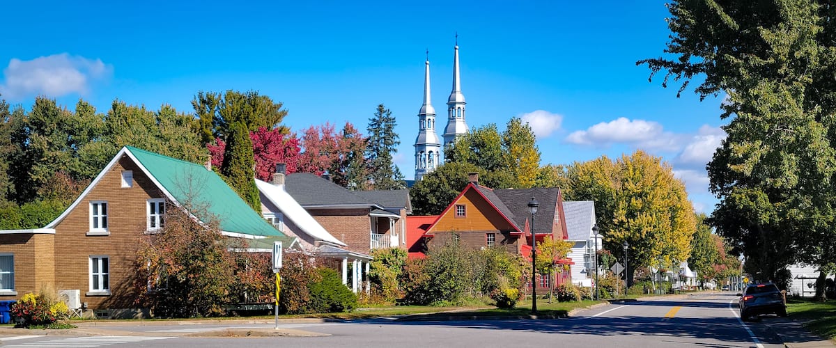 A street with houses, a church with two spires, and autumn-colored trees.