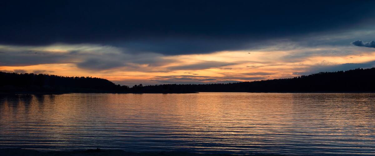 A sunset over a calm lake with a forested shoreline.