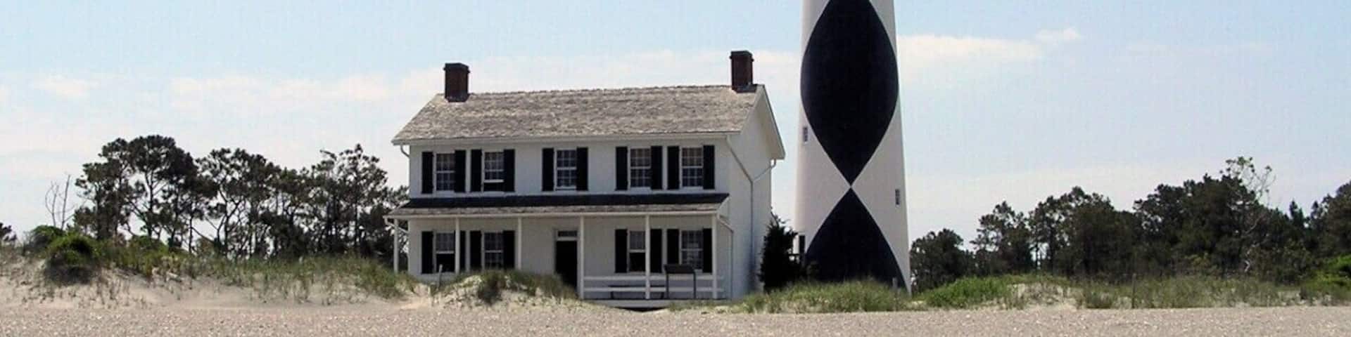 A beach with a white house and a black and white lighthouse.