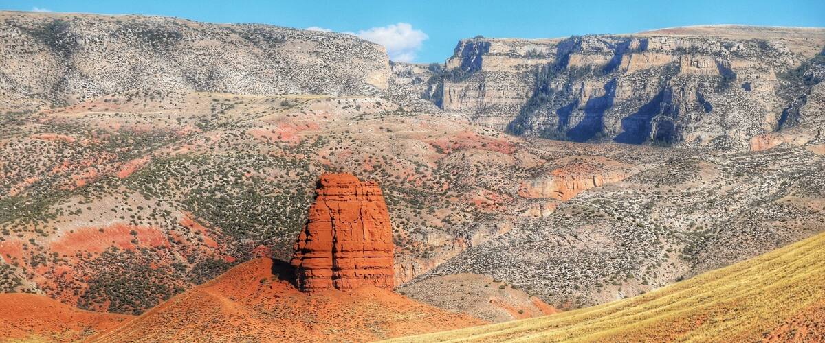 A red rock formation, a steep cliff, and a valley with sparse vegetation.