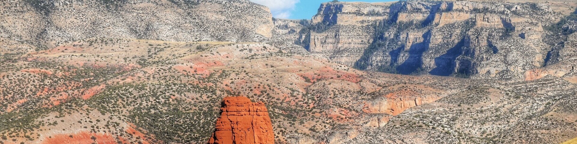 A red rock formation, a steep cliff, and a valley with sparse vegetation.