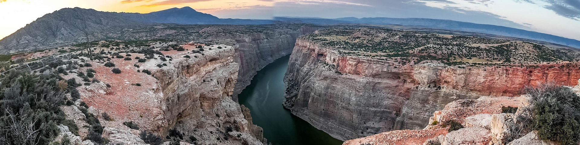 Ein tiefes Canyons mit einem Fluss, umgeben von Bergen und spärlicher Vegetation.