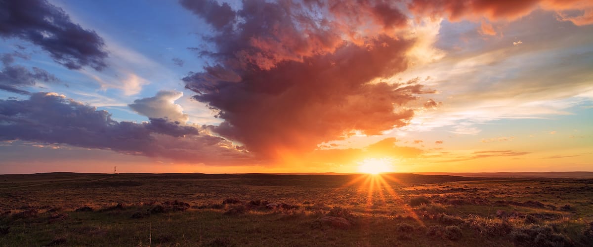 A sunset over a flat landscape with a prominent cloud formation.