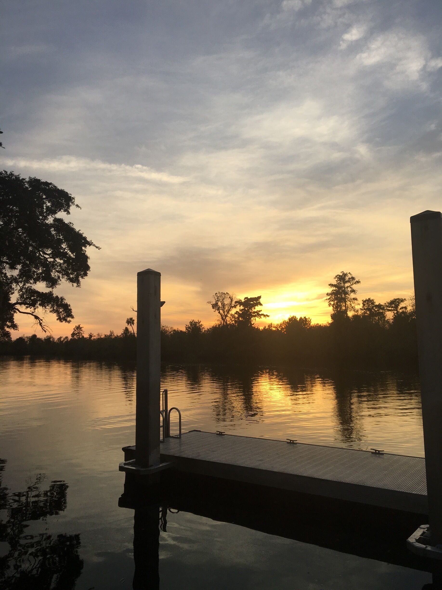 A sunset over a calm lake with a dock and trees in the background.