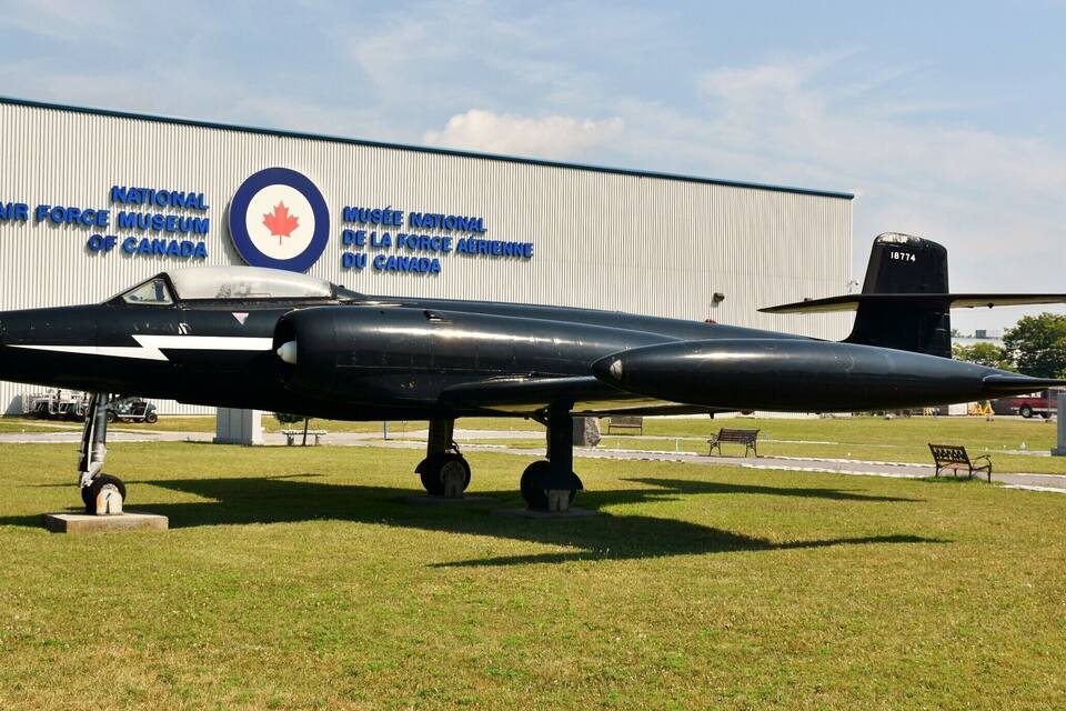 A black military aircraft on display in front of a building with a Canadian flag and the text "National Air Force Museum of Canada".