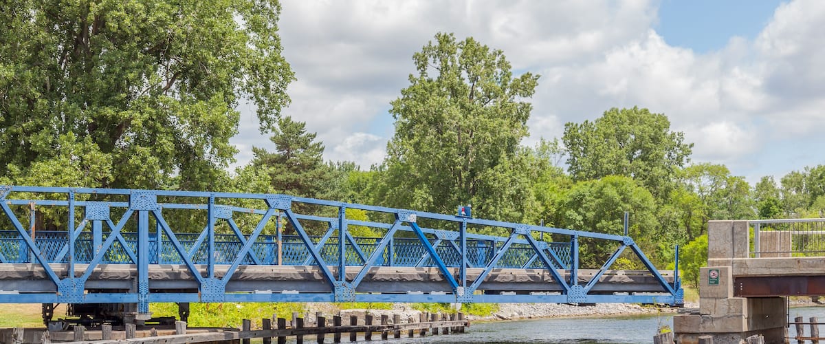 A blue steel bridge over a river with trees in the background.
