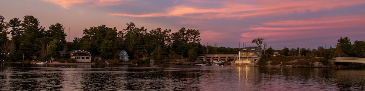 Un lac paisible, avec un coucher de soleil, un pont et des maisons qui bordent la rive.