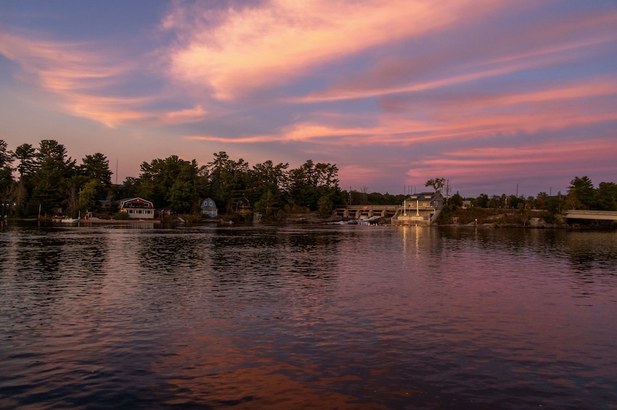 A calm lake with a sunset, a bridge, and houses along the shore.