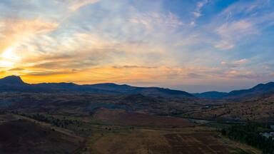 A mountainous landscape with a river and a sunset.