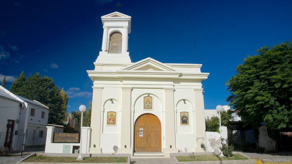 A white church with a bell tower, arched door, and religious paintings.