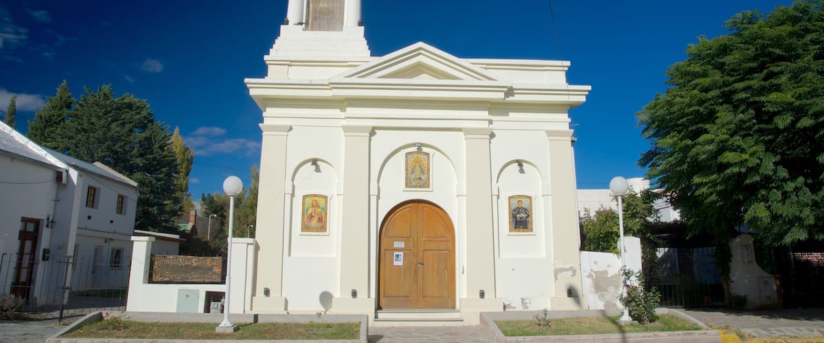 A white church with a bell tower, arched door, and religious paintings.
