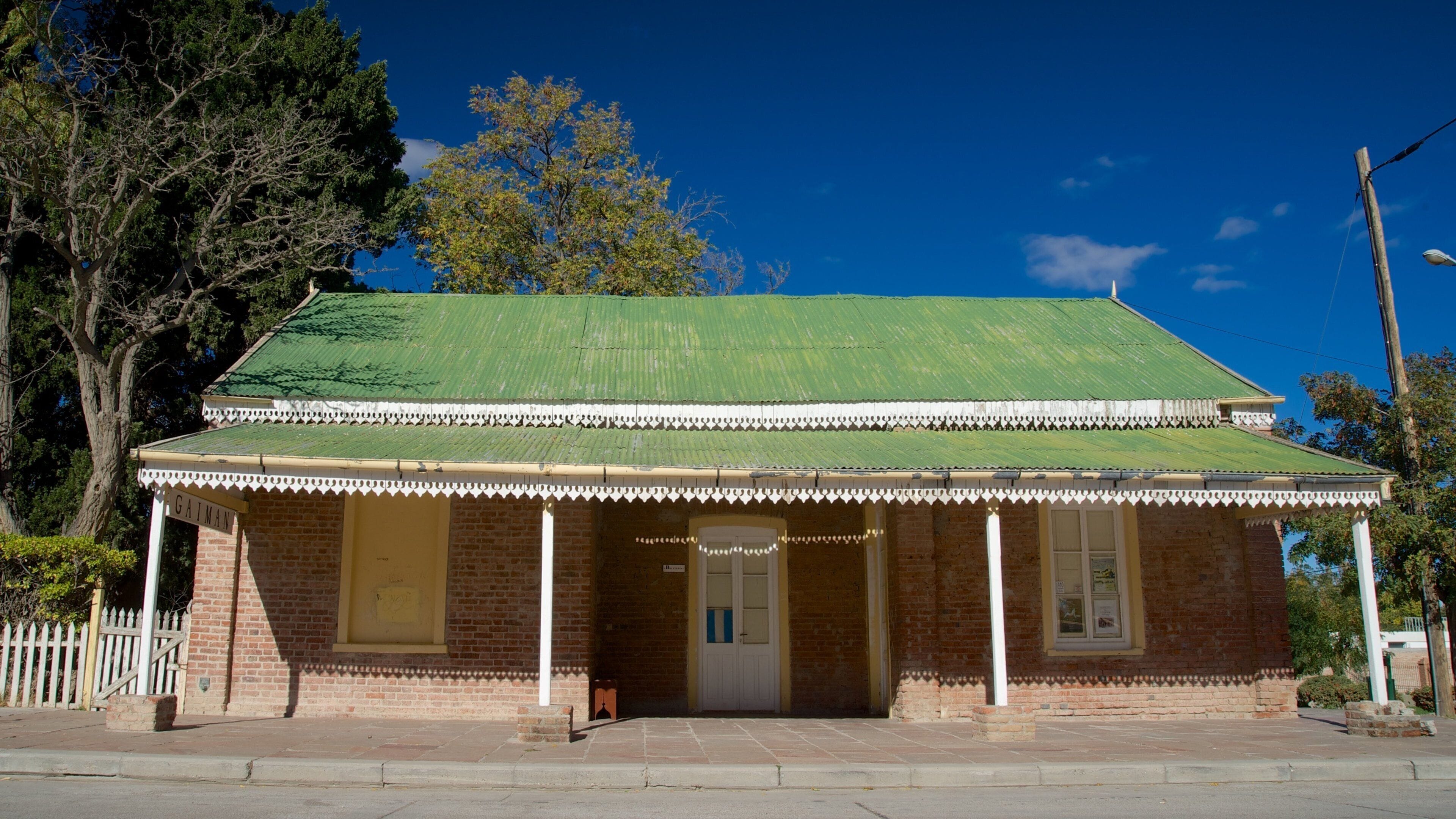 A brick building with a green roof and a white picket fence.