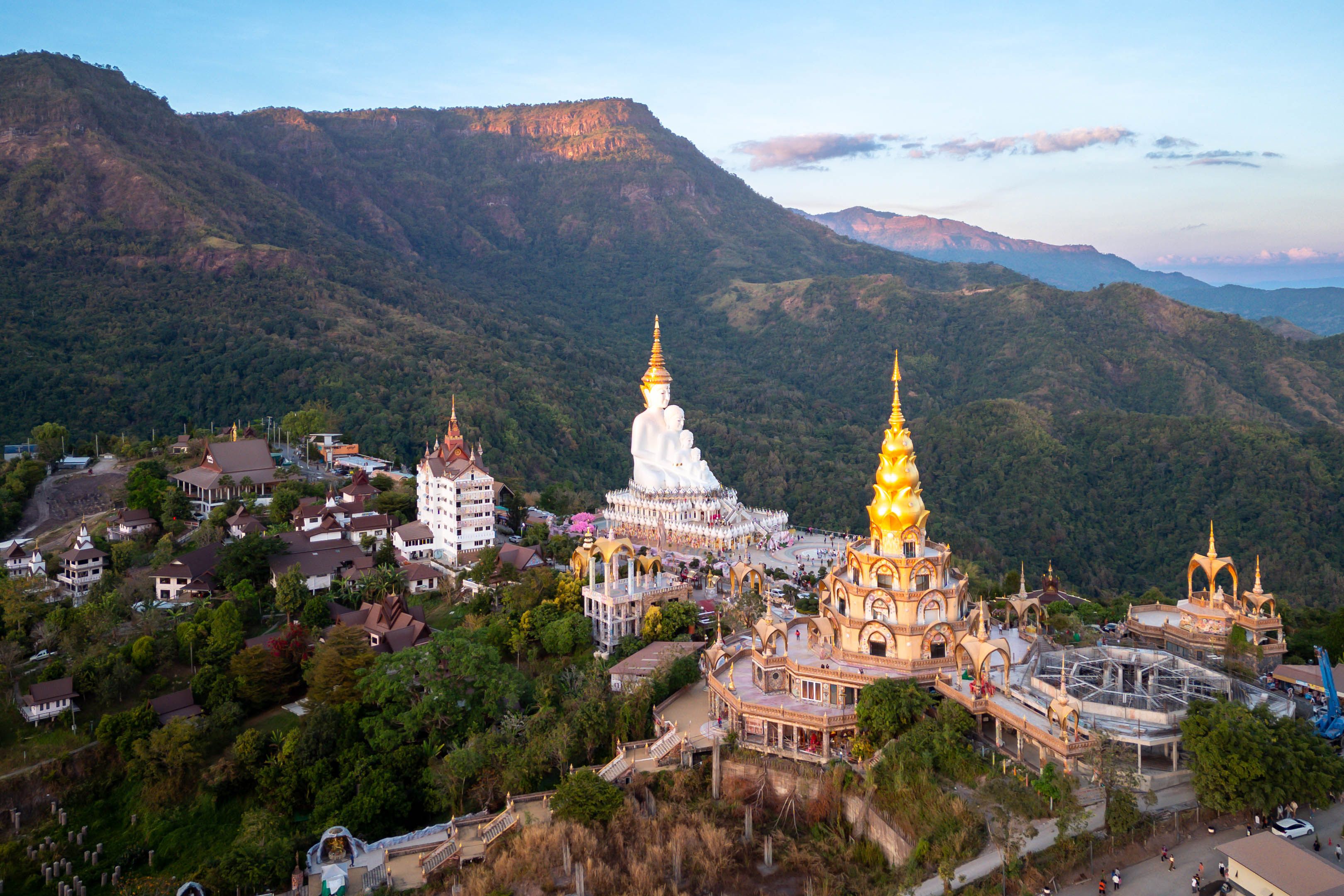Un paysage montagneux avec un ensemble de temples caractérisé par des flèches dorées et des dômes blancs.
