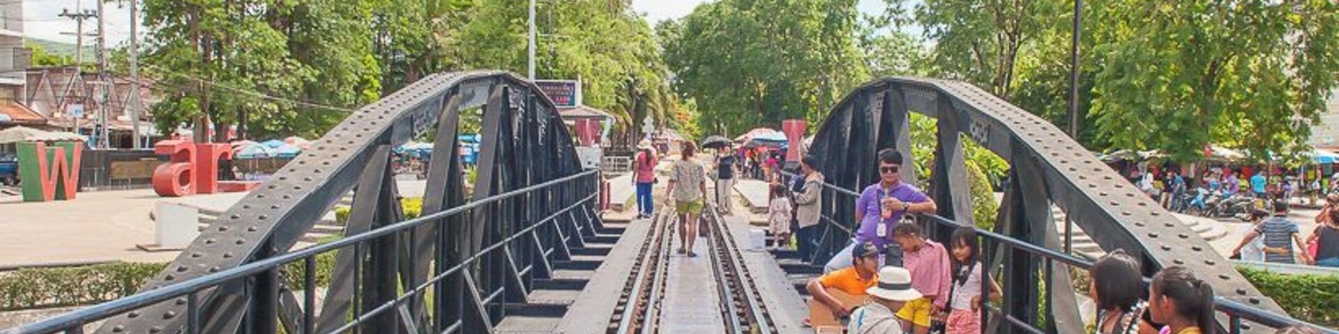 Uma ponte de aço com trilhos, rodeada por árvores e pessoas.