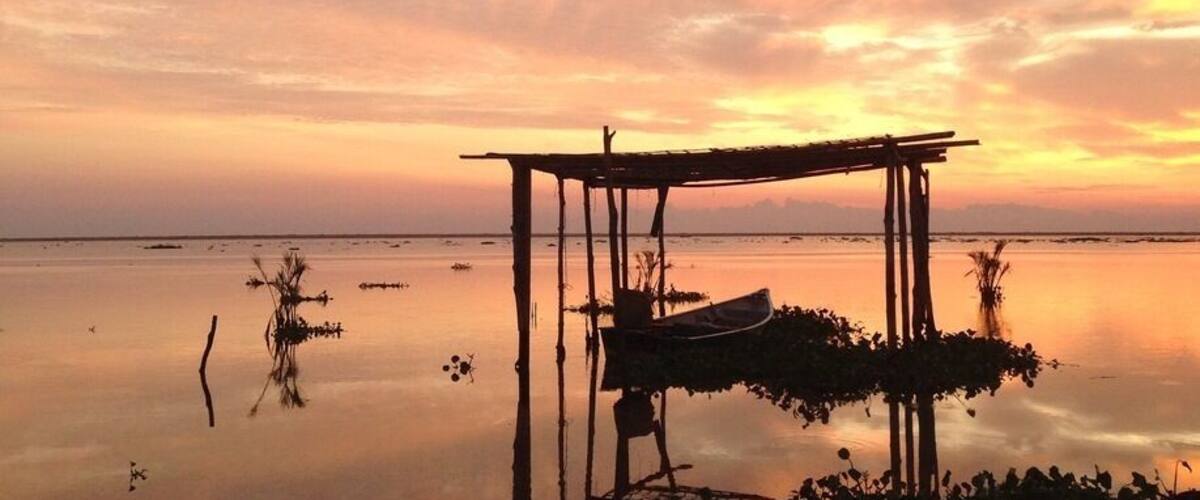 A wooden structure on a calm body of water during sunset.