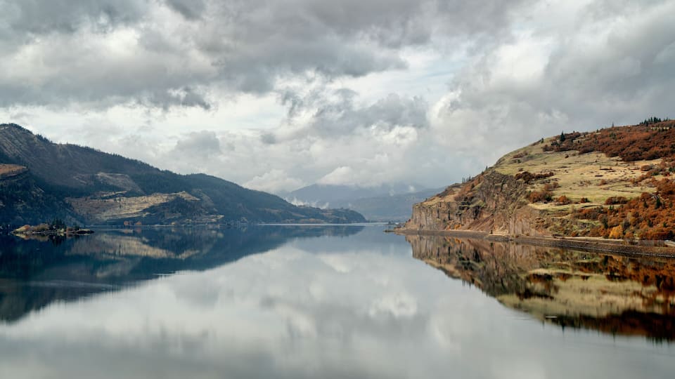 A calm lake reflecting mountains and a cloudy sky.