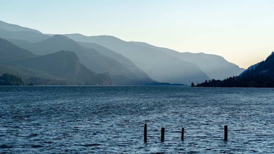 A calm lake with mountains in the background and wooden posts in the water.